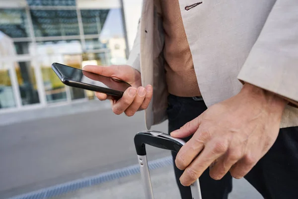 Hands of man holding smartphone and suitcase handle — Stock Photo, Image