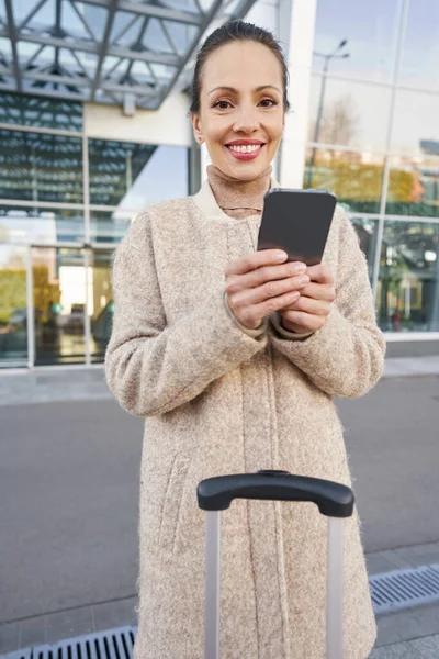 Mulher positiva olhando para a câmera enquanto segura o smartphone — Fotografia de Stock