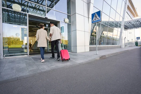 Två personer in på flygplatsen med väska på hjul bakom dem — Stockfoto