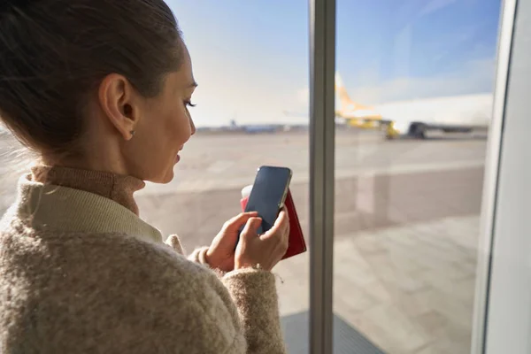女性クリック彼女のスマートフォン近くの空港ウィンドウ — ストック写真