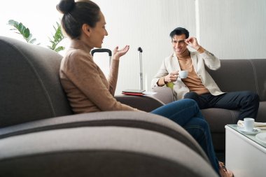 Kahveli adam ve koltuklarda oturan kadın.