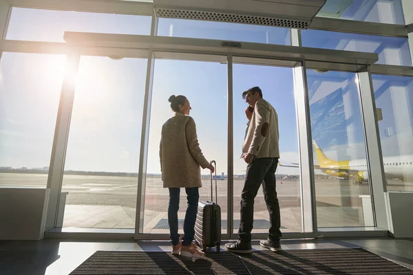 Mężczyzna na telefonie i kobieta z walizką na lotnisku — Zdjęcie stockowe