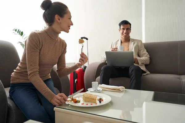 Woman eating cake and looking at man with laptop — Stock Photo, Image