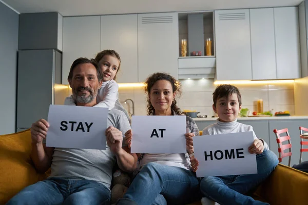 Pleased family showing paper signs to camera from sofa — Stock Photo, Image