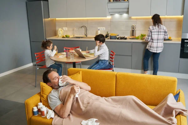 Kranker Mann auf Sofa neben seiner Familie in Küche — Stockfoto