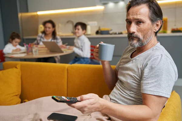 Спокойный человек на диване с чаем и нажатием на пульт дистанционного управления — стоковое фото