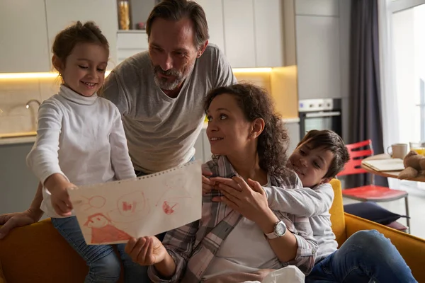 Mulher com criança no sofá demonstrando desenho para sua família — Fotografia de Stock