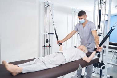 Kanepede uzanmış yaşlı bir kadın halatla ağırlık çekiyor.