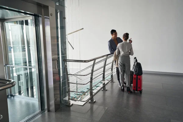 Zwei Personen mit Gepäck unterhalten sich in der Nähe von Aufzug im Flur — Stockfoto