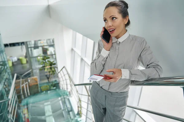 Stylish woman with travel documents talking on smartphone on staircase — Stock Photo, Image