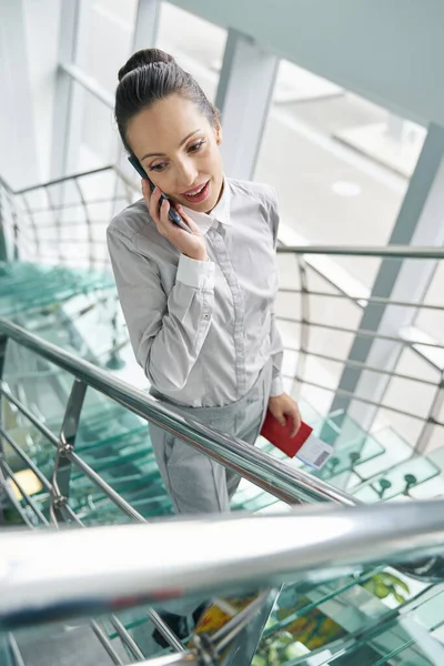 Female with travel documents having phone conversation on glass stairs — Stock Photo, Image