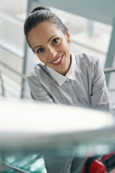 Joyful lady with baggage posing for camera on glass stairs — Stock Photo, Image