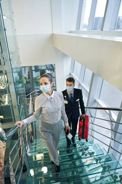 Elegant lady with travel document and bellboy going up stairs — Stock Photo, Image