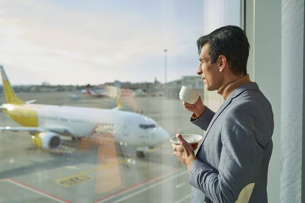 Männlicher Passagier mit Getränken steht im Wartebereich des Flughafens — Stockfoto