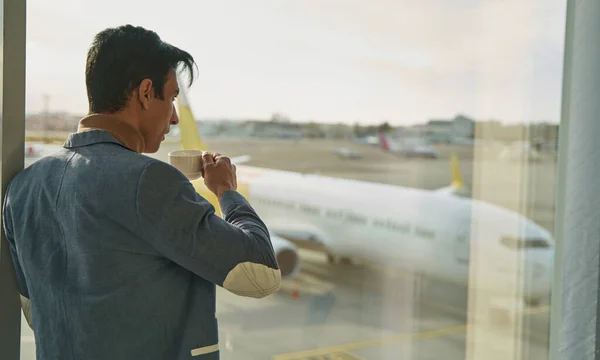 Hombre con taza de café de pie junto a la ventana en el salón del aeropuerto —  Fotos de Stock