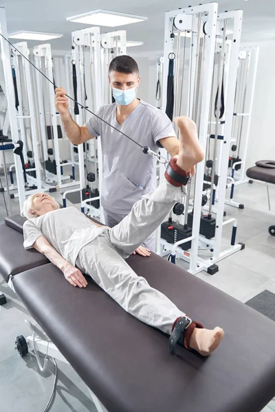 Pensionista levantando perna com alça de tornozelo durante o treino da máquina de cabo — Fotografia de Stock