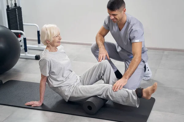 Terapist, yaşlı kadın bacağını egzersize hazırlıyor. — Stok fotoğraf