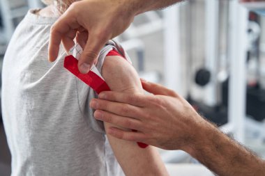 Erkek doktor emeklilerin koluna kırmızı kinesiyoloji bandı yapıştırıyor.
