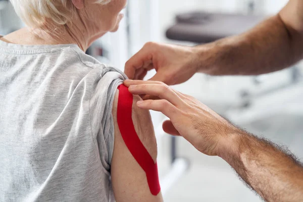Lékařský pracovník zmírnění bolesti ramene s elastickou terapeutickou páskou — Stock fotografie