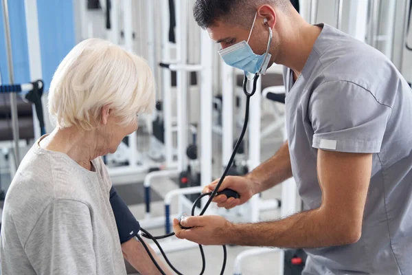 Médico usando medidor de pressão arterial no braço da mulher envelhecida — Fotografia de Stock