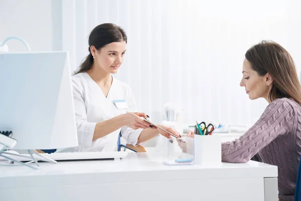 Woman affixing signature to document in doctor office — Stock Photo, Image