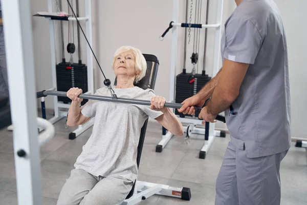 Old lady pulling weight on training equipment with hands — Stock Photo, Image