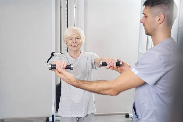Professionell fysioterapeut maning äldre kvinnliga händer med hantlar — Stockfoto