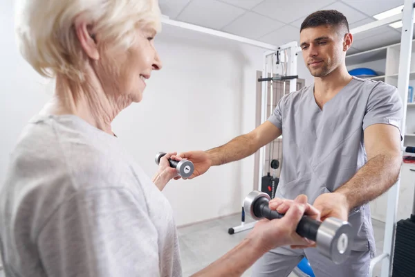 Physiotherapeutin hilft Rentnerin beim Hantelheben — Stockfoto