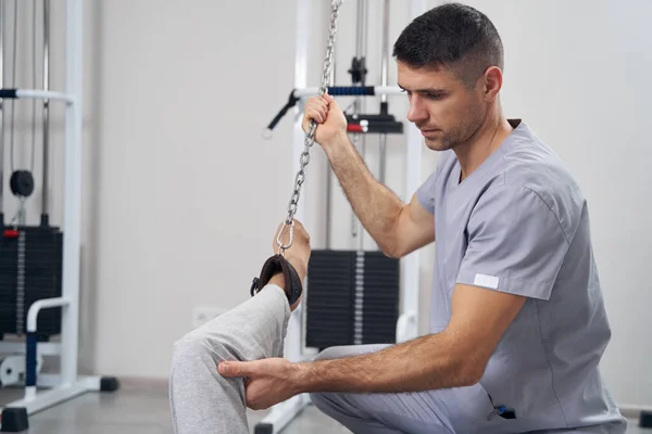 Ortopedista segurando perna pessoa durante o exercício da máquina de cabo — Fotografia de Stock