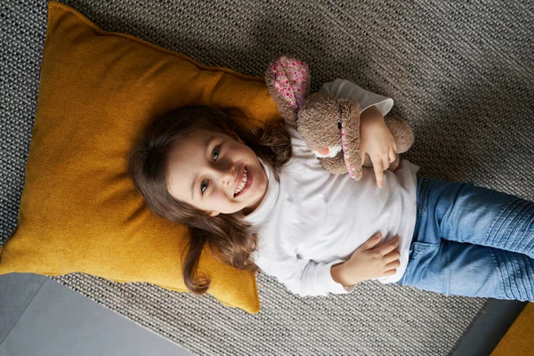 Χαρούμενο κορίτσι που χαρίζει ένα χαμόγελο στην κάμερα από το πάτωμα — Φωτογραφία Αρχείου