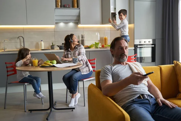 Apa TV-t néz, miközben anya a konyhában dolgozik a gyerekek közelében — Stock Fotó
