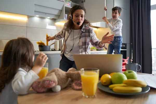 Mujer con llamada de negocios mientras cocina y calma a los niños —  Fotos de Stock