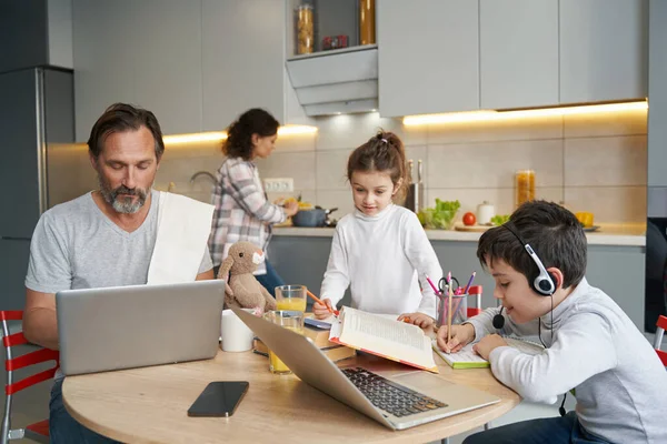 Сім'я на кухні працює з домашнім завданням і ноутбуком за столом — стокове фото