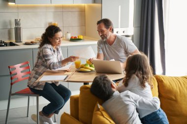 Çocuklar ararken ebeveynler mutfakta vergi işleriyle uğraşıyor.