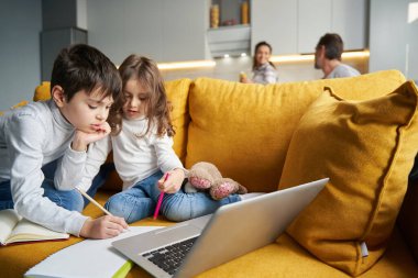 Erkek ve kız kardeş kanepede ödev yapıyor.