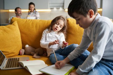 Çocuk kız kardeşiyle birlikte not defterine ödevlerini yazıyor.