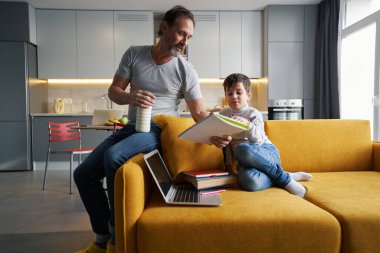 Ebeveyn kanepeye oturur ve çocuğa ödevlerinde yardım eder.