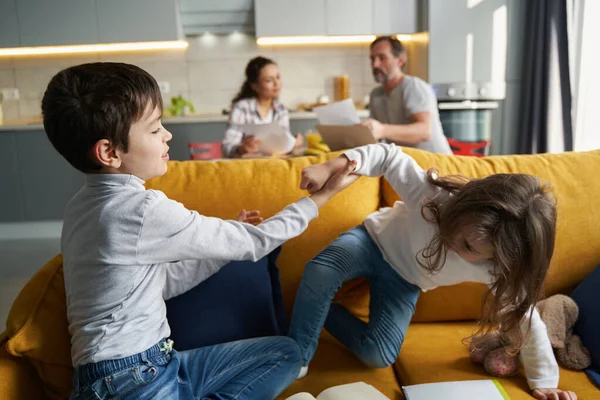 Crianças brincando no sofá com os pais no fundo — Fotografia de Stock