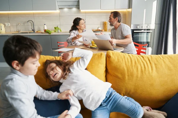Niños peleando en el sofá mientras sus padres trabajan —  Fotos de Stock