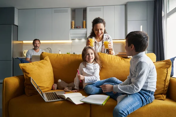 Madre positiva trayendo jugo de naranja a los niños en el sofá — Foto de Stock