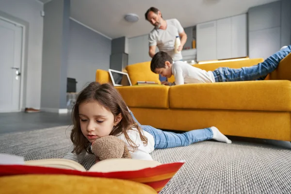 Uważne czytanie książki dla dzieci na podłodze przed sofą — Zdjęcie stockowe
