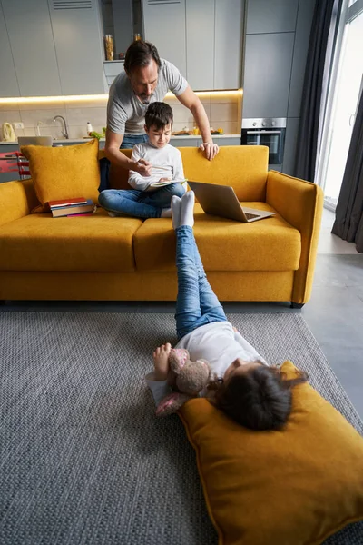 Junge und Vater machen Hausaufgaben, während Mädchen auf dem Boden liegt — Stockfoto