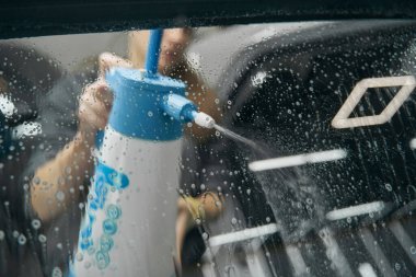 Kadın sprey şişeden oto cam yüzeyine temizlik solüsyonu uyguluyor.