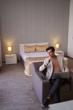 Dizüstü bilgisayarı olan düşünceli beyefendi odada oturuyor.