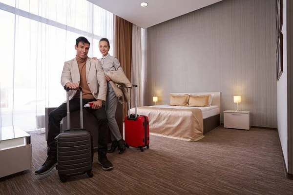 Joyous couple with trolley suitcases in hotel room — Stock Photo, Image