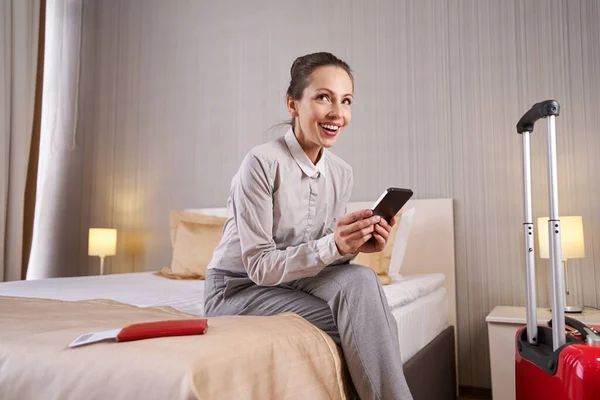 Mulher alegre sentada com celular no quarto de hotel — Fotografia de Stock