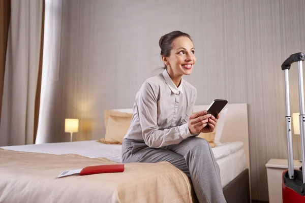 Happy female tourist with smartphone sitting in her suite — Stock Photo, Image