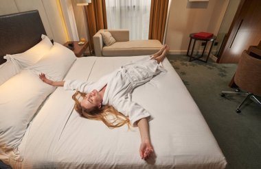 Yatakta yatarken kollarını açan rahat bir kadın.