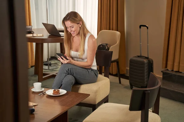 Fröhliches Tippen auf dem Smartphone im Sitzen in Hotelsuite — Stockfoto