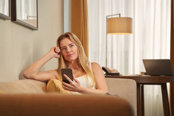 Žena sní na gauči, zatímco drží smartphone — Stock fotografie